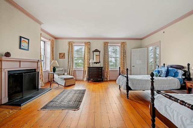 bedroom featuring light wood-style floors, crown molding, and a fireplace with raised hearth