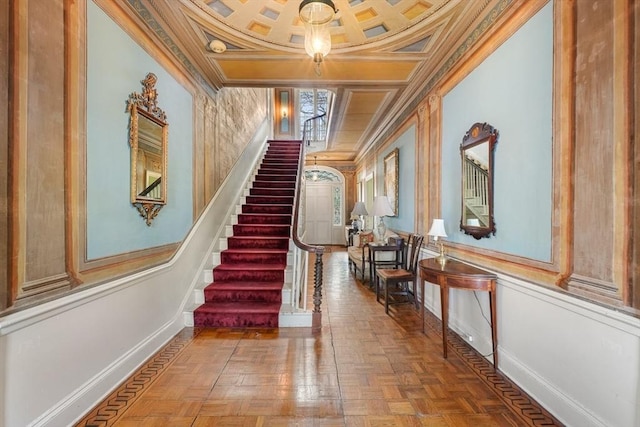 stairs featuring crown molding, coffered ceiling, baseboards, and a decorative wall
