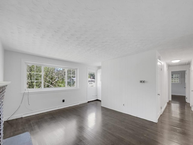 unfurnished living room featuring a textured ceiling, dark hardwood / wood-style flooring, and a stone fireplace