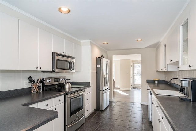 kitchen with a sink, backsplash, dark countertops, and appliances with stainless steel finishes