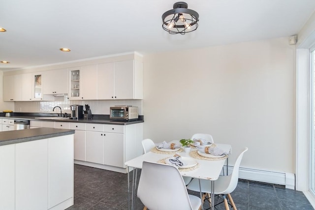 kitchen with dark countertops, backsplash, dishwasher, white cabinetry, and a sink