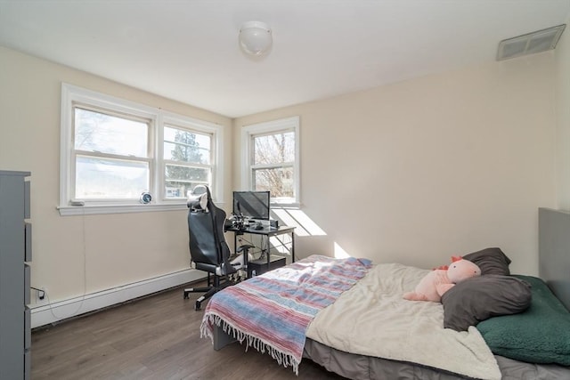 bedroom with visible vents, wood finished floors, and a baseboard heating unit