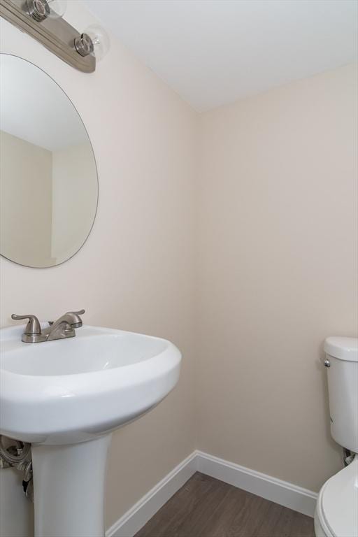 half bath with toilet, wood finished floors, and baseboards