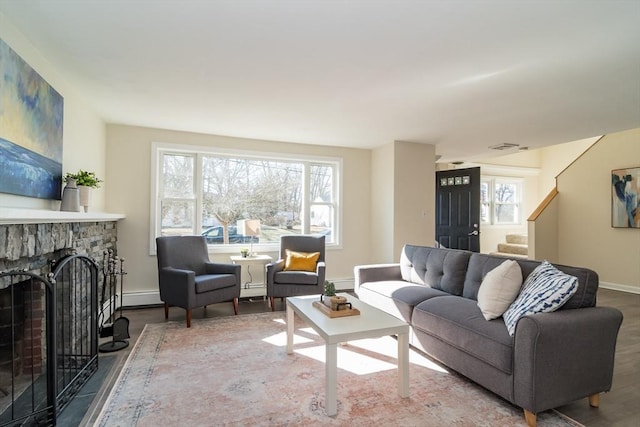 living area with wood finished floors, a fireplace, a baseboard radiator, baseboards, and stairs