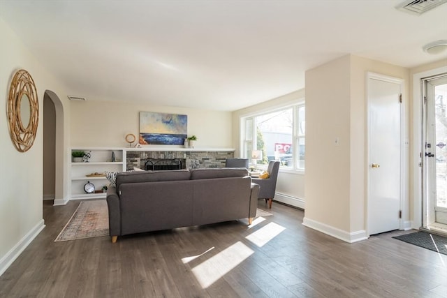 living room featuring visible vents, a fireplace, arched walkways, dark wood-type flooring, and a baseboard heating unit