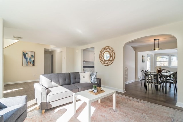 living room with arched walkways, visible vents, baseboards, and wood finished floors