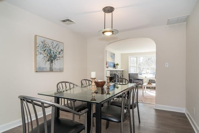 dining area with dark wood-style floors, visible vents, baseboards, arched walkways, and a stone fireplace