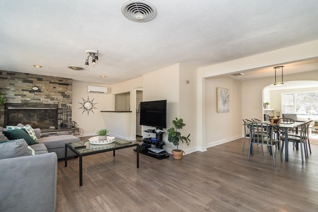 living room with visible vents, a stone fireplace, baseboards, and wood finished floors