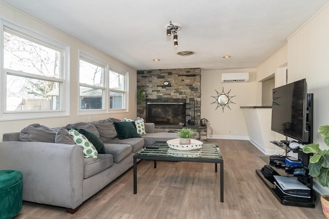 living room featuring wood finished floors, visible vents, baseboards, a fireplace, and a wall mounted air conditioner