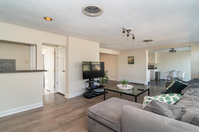 living area featuring visible vents, baseboard heating, dark wood-type flooring, and baseboards