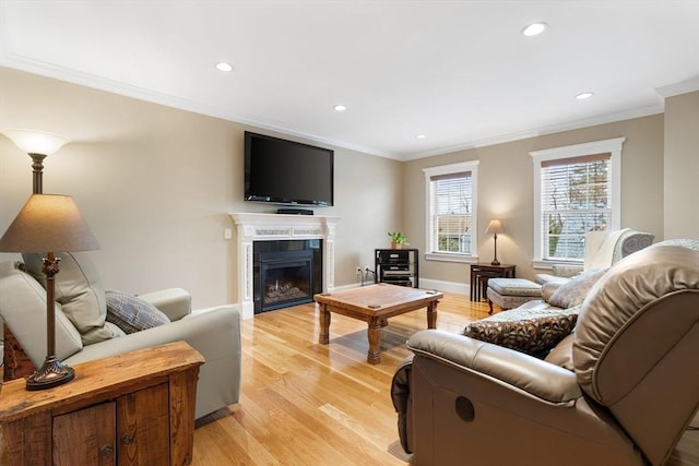 living area with a glass covered fireplace, light wood-style flooring, recessed lighting, and ornamental molding