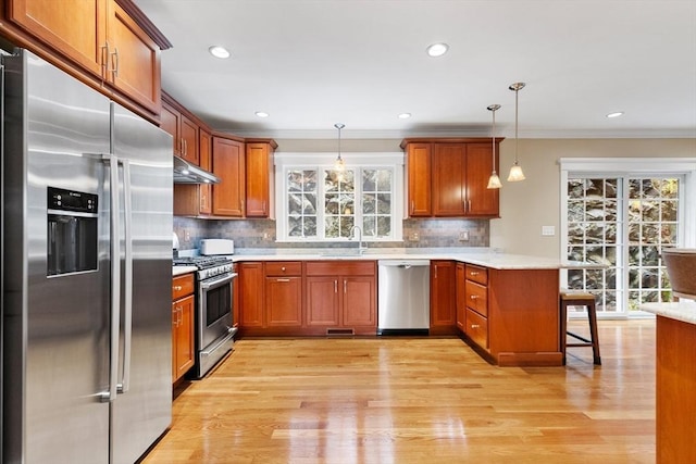 kitchen with a peninsula, brown cabinetry, appliances with stainless steel finishes, and under cabinet range hood