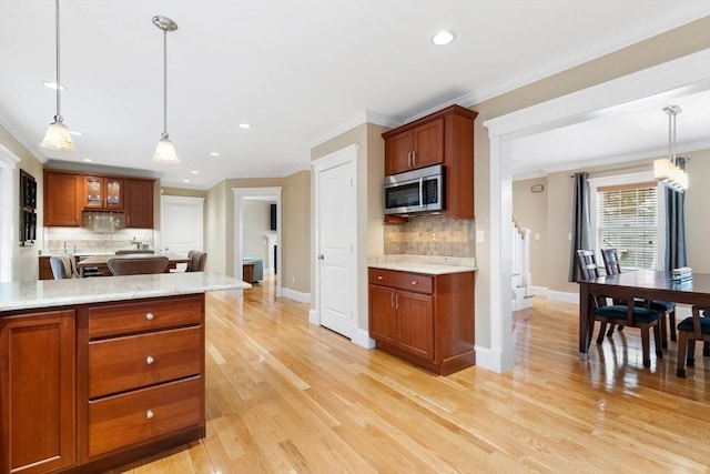 kitchen with stainless steel microwave, brown cabinets, ornamental molding, and light wood finished floors