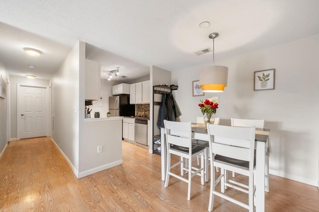 dining room with light wood-type flooring, visible vents, and baseboards