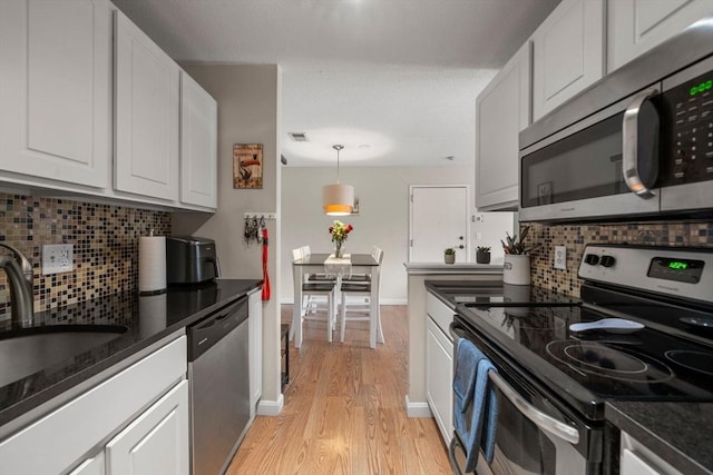 kitchen with appliances with stainless steel finishes, white cabinetry, a sink, and light wood-style flooring