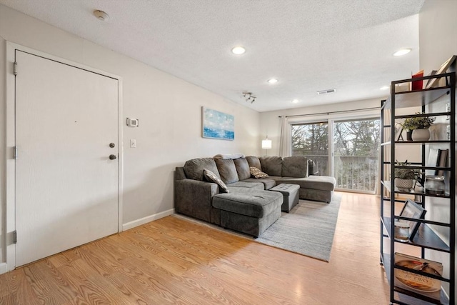 living room with a textured ceiling, recessed lighting, wood finished floors, visible vents, and baseboards