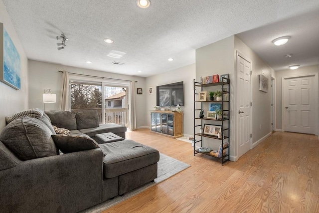 living room with recessed lighting, visible vents, light wood-style flooring, a textured ceiling, and baseboards