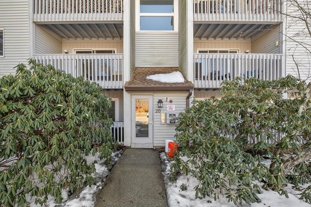 view of exterior entry featuring a shingled roof and a balcony