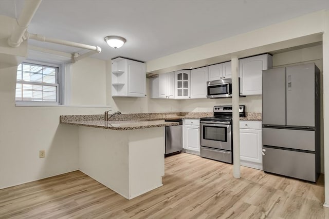 kitchen with white cabinets, kitchen peninsula, stainless steel appliances, light stone countertops, and light hardwood / wood-style flooring