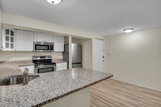 kitchen with white cabinets, light stone counters, kitchen peninsula, stainless steel appliances, and light hardwood / wood-style floors