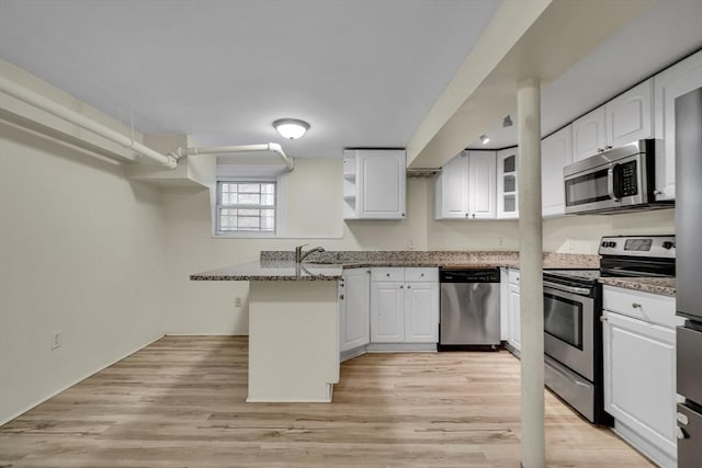 kitchen with stainless steel appliances, white cabinetry, dark stone countertops, and kitchen peninsula