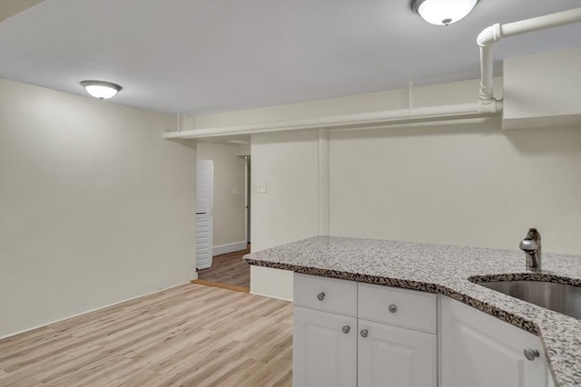 kitchen with white cabinetry, sink, light stone counters, and light hardwood / wood-style floors