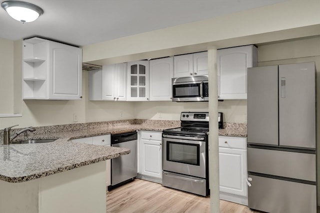 kitchen with appliances with stainless steel finishes, white cabinets, light stone counters, kitchen peninsula, and light wood-type flooring