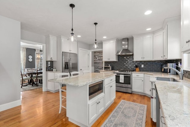 kitchen featuring pendant lighting, white cabinets, built in appliances, and wall chimney range hood