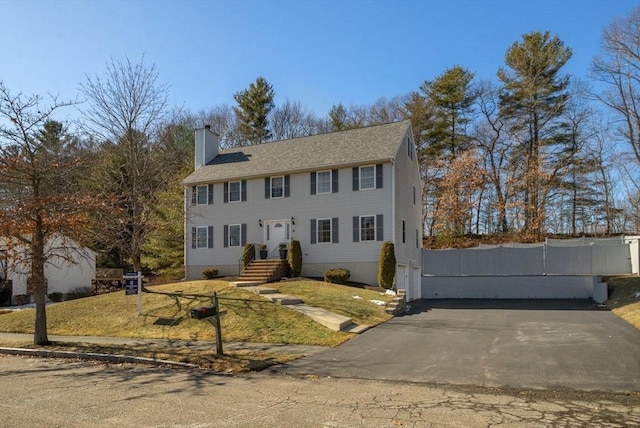 colonial home featuring driveway, a chimney, and fence