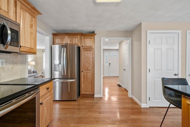 kitchen with stainless steel appliances, baseboards, decorative backsplash, light wood finished floors, and dark countertops