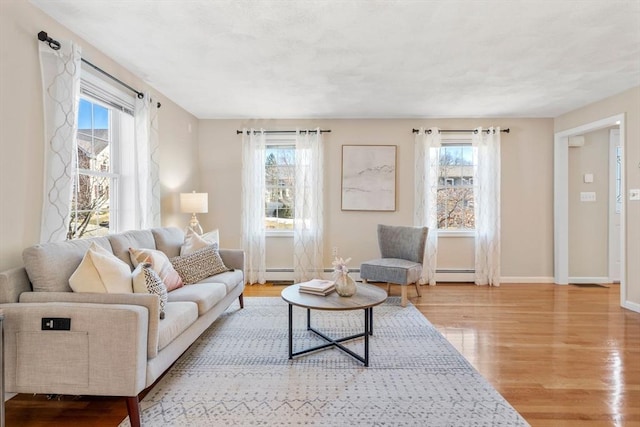 living area featuring a baseboard heating unit, wood finished floors, and baseboards