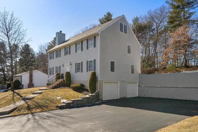 colonial inspired home with driveway, a chimney, and an attached garage