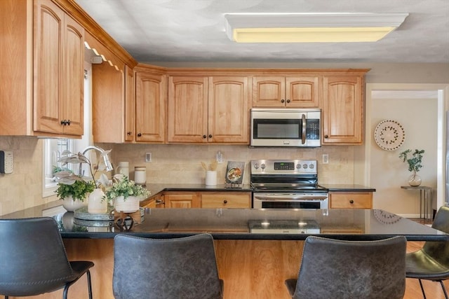 kitchen featuring stainless steel appliances, a peninsula, decorative backsplash, dark countertops, and a kitchen bar