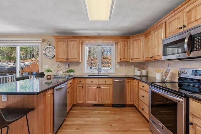 kitchen featuring tasteful backsplash, appliances with stainless steel finishes, a peninsula, light wood-style floors, and a sink