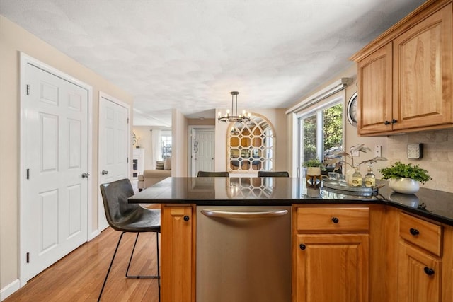 kitchen featuring dark countertops, decorative backsplash, light wood-style floors, a peninsula, and a kitchen breakfast bar