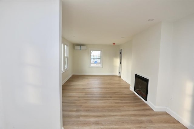 unfurnished living room featuring a wall unit AC and light hardwood / wood-style floors