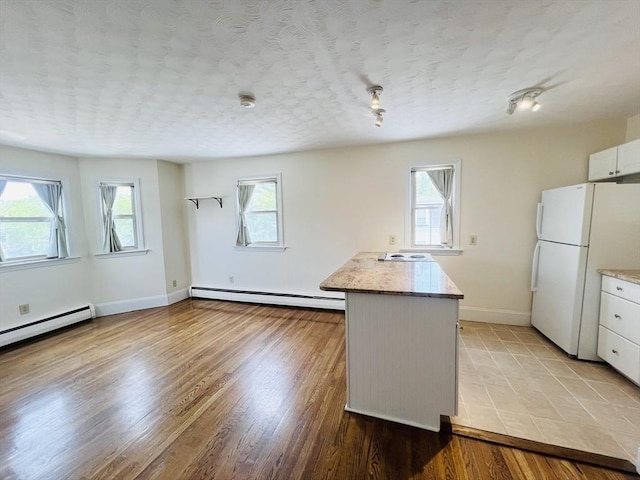 189 Concord Ave Unit 3, Cambridge, MA 02138 - kitchen with freestanding refrigerator, a baseboard heating unit, plenty of natural light, and white cabinets