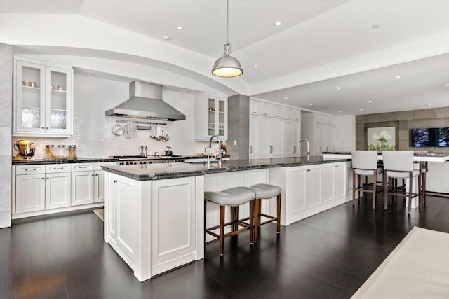 1014 Boylston St, Brookline, MA 02467 - kitchen featuring wall chimney range hood, glass insert cabinets, dark stone counters, a sink, and recessed lighting