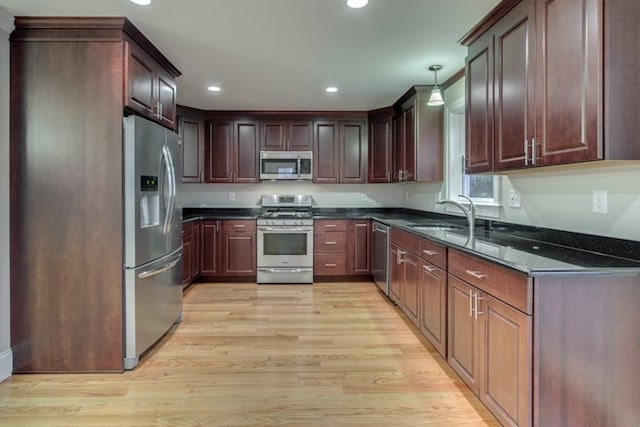 kitchen featuring dark stone countertops, appliances with stainless steel finishes, light hardwood / wood-style flooring, and sink