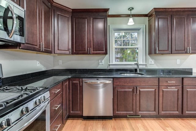 kitchen featuring light wood-type flooring, dark stone counters, crown molding, sink, and appliances with stainless steel finishes