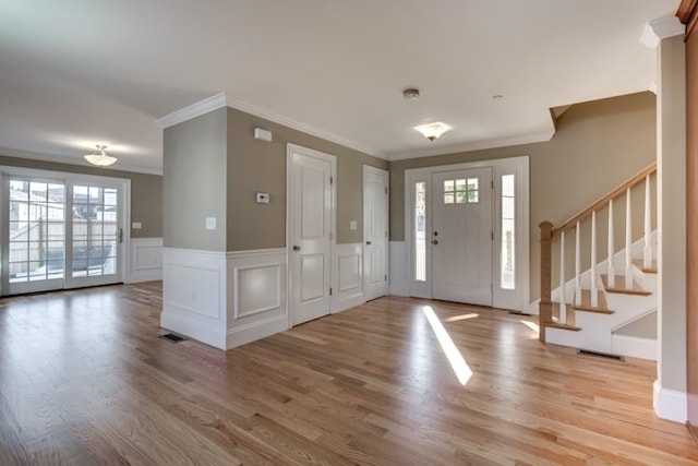 foyer entrance with ornamental molding, a wealth of natural light, and light hardwood / wood-style floors