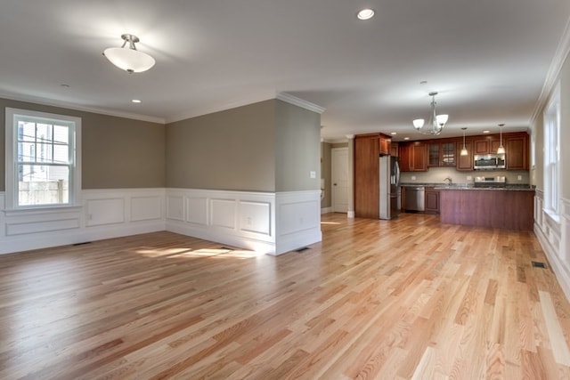 unfurnished living room with light wood-type flooring, ornamental molding, and an inviting chandelier