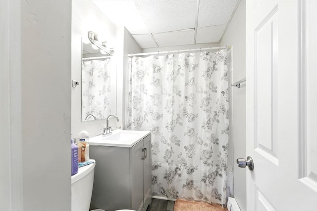 bathroom featuring baseboard heating, vanity, curtained shower, a drop ceiling, and toilet