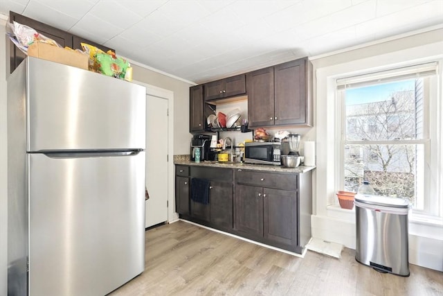 kitchen with a sink, dark brown cabinetry, appliances with stainless steel finishes, light wood finished floors, and ornamental molding