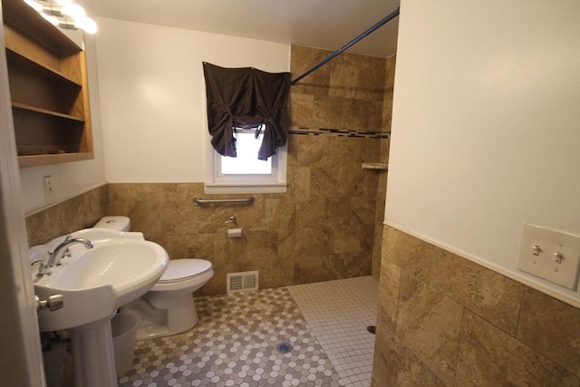 bathroom featuring a tile shower, tile patterned floors, tile walls, and toilet