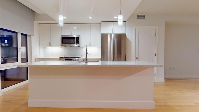 kitchen with stainless steel appliances, sink, decorative light fixtures, white cabinets, and an island with sink