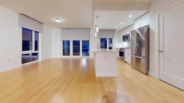 kitchen with hanging light fixtures, white cabinets, light hardwood / wood-style floors, a kitchen island, and appliances with stainless steel finishes