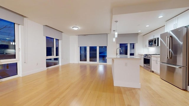 kitchen with light wood-type flooring, white cabinetry, hanging light fixtures, and appliances with stainless steel finishes