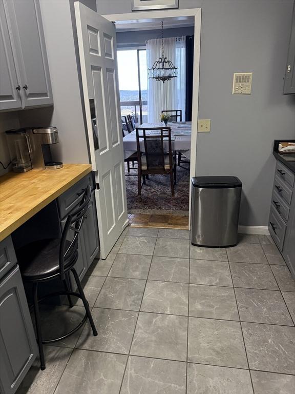 kitchen with light tile patterned floors, gray cabinets, a notable chandelier, and wood counters