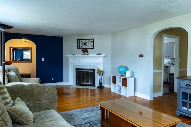 living area featuring arched walkways, wood finished floors, a fireplace with flush hearth, and baseboards